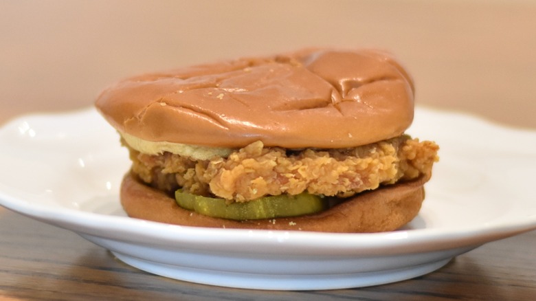 A Popeyes chicken sandwich with golden barbecue sauce and pickles on a white plate