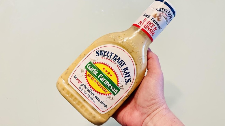 Hand holding bottle of Sweet Baby Ray's Garlic Parmesan Sauce & Marinade