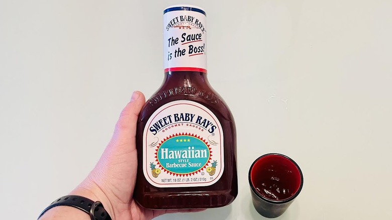 Hand holding bottle of Sweet Baby Ray's Hawaiian Style Barbecue Sauce with small serving on side