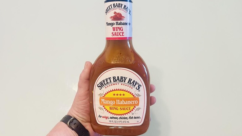 Hand holding bottle of Sweet Baby Ray's Mango Habanero Buffalo Wing Sauce
