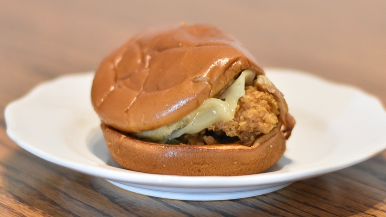 A Popeyes spicy chicken sandwich with cheese and bacon on a white plate