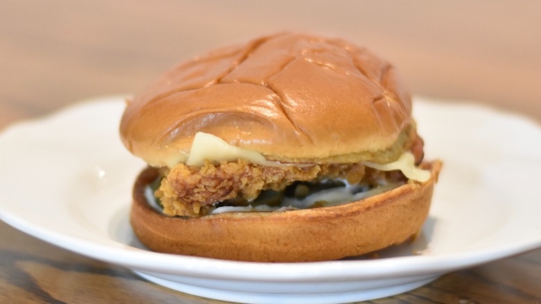 A Popeyes chicken sandwich with mayo, pickles, cheese, and bacon on a white plate