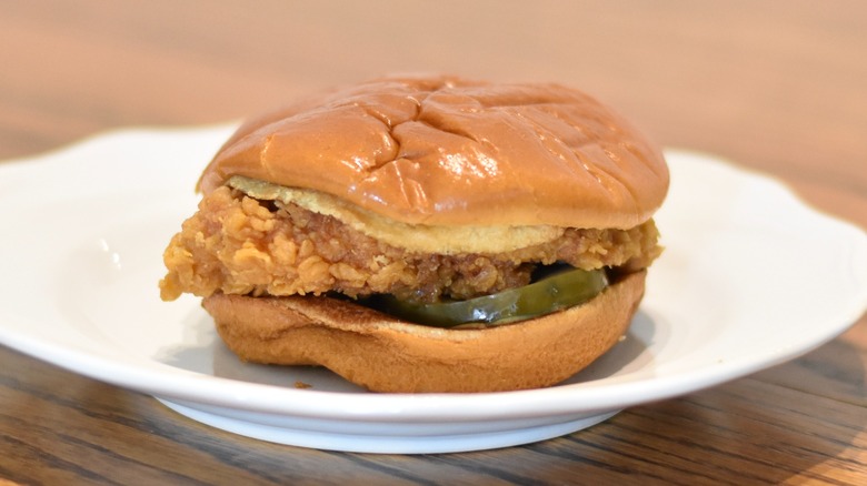 A Popeyes spicy chicken sandwich with pickles on a white plate