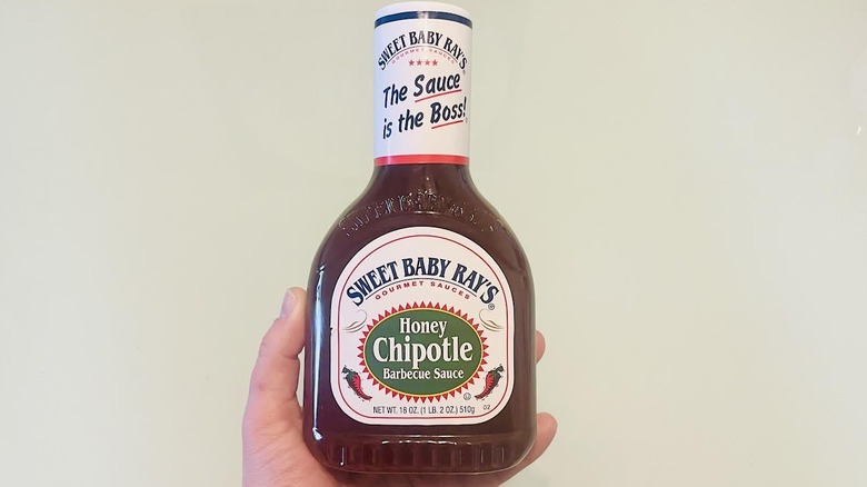 Hand holding bottle of Sweet Baby Ray's Honey Chipotle Barbecue Sauce