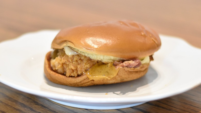 A Popeyes chicken sandwich with ghost pepper sauce and cheese on a white plate