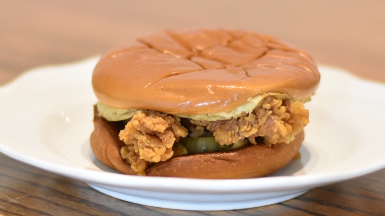 A Popeyes ghost pepper chicken sandwich with pickles on a white plate