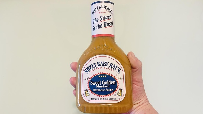 Hand holding bottle of Sweet Baby Ray's Sweet Golden Mustard Barbecue Sauce