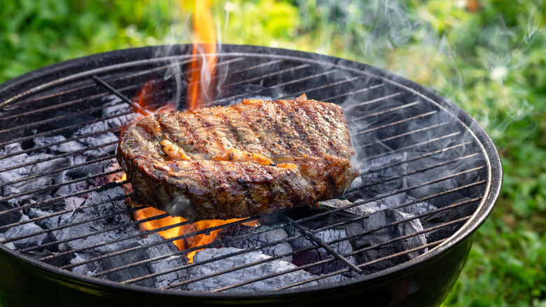 A steak cooking on a charcoal grill