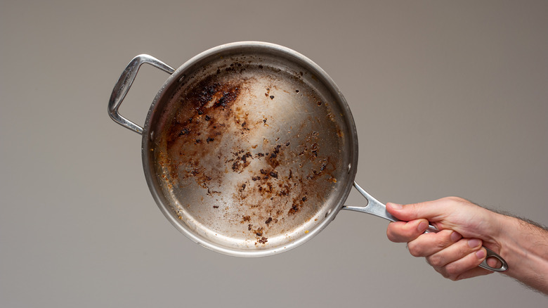 An individual holding a dirty metal frying pan.