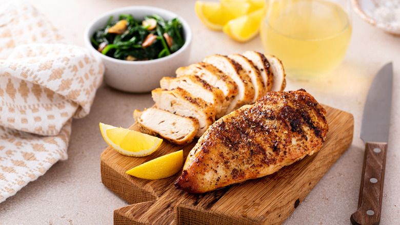 Lemon chicken on wooden board with bowl of greens