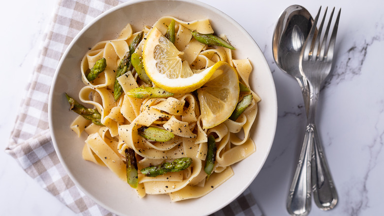 Lemon pasta with asparagus and silverware on marble surface
