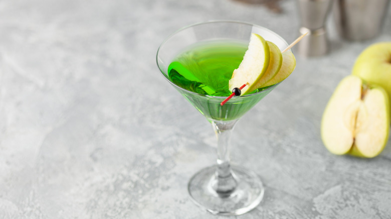 A neon green drink in a martini glass garnished with apple slices