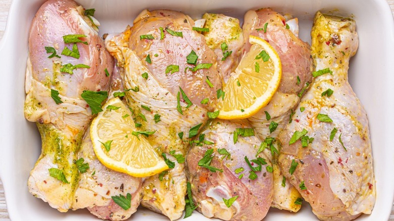 Marinating raw chicken drumsticks with lemon and herbs