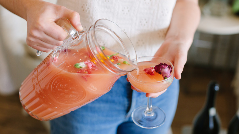 A person pouring a cocktail from a pitcher into a glass