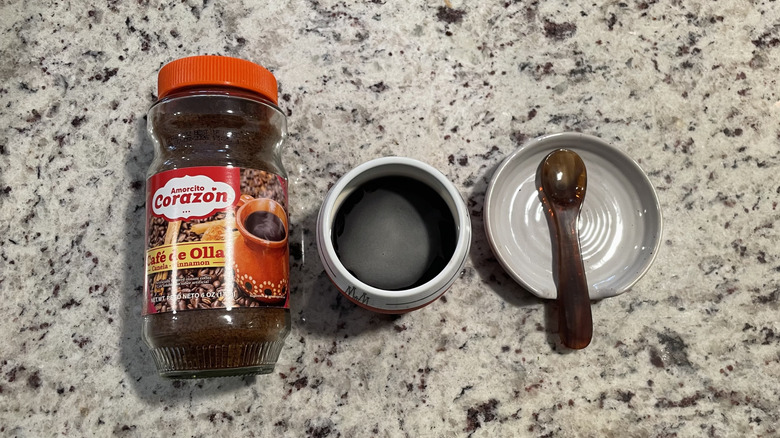 Amorcito Corazon coffee packaging is next to a cup of coffee and a spoon on a saucer.