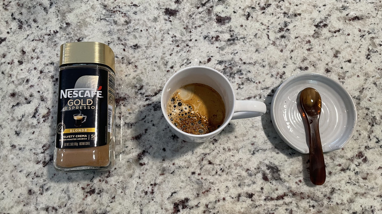 Nescafe coffee packaging is next to a cup of coffee and a spoon on a saucer.