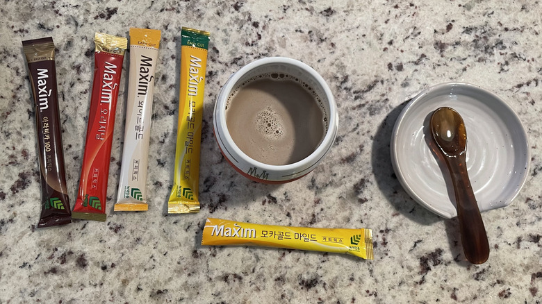 Assorted Maxim coffees are shown next to a cup of coffee and a spoon on a saucer.