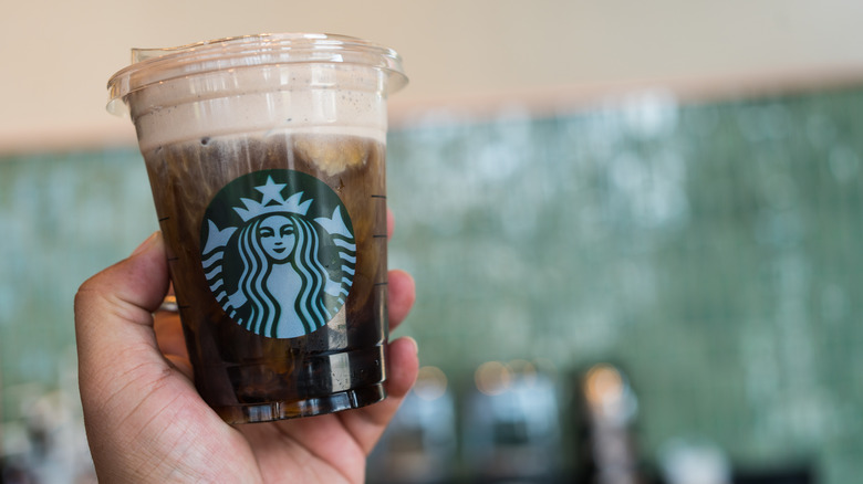 A person holding an iced coffee topped with cold foam in a Starbucks takeaway cup