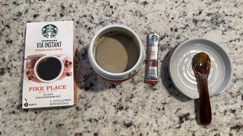 Starbucks Via Instant Coffee packaging is next to a cup of coffee and a spoon on a saucer.