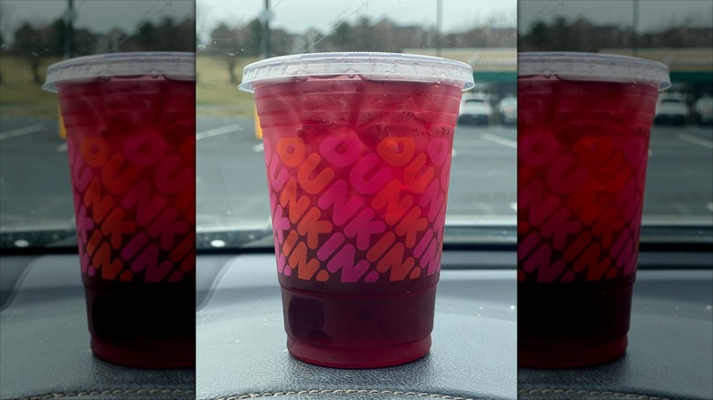A Dunkin' Blueberry Pomegranate Refresher sitting on a car's dashboard