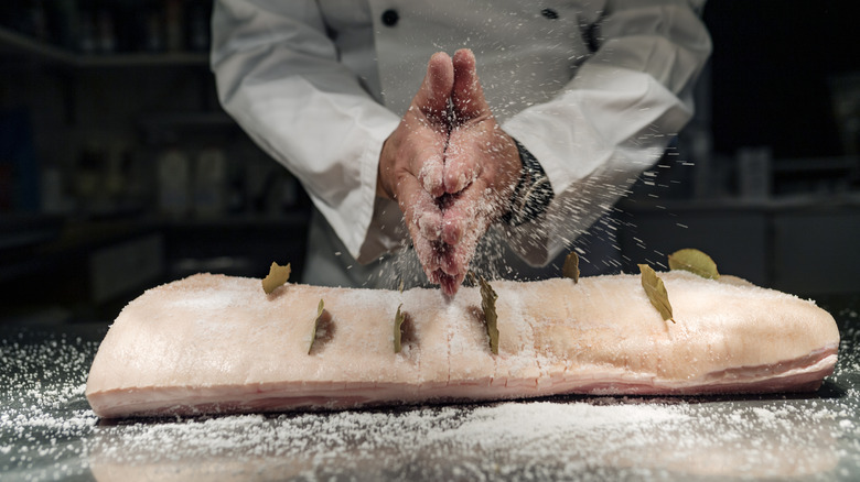 man sprinkles slat over large cut of pork
