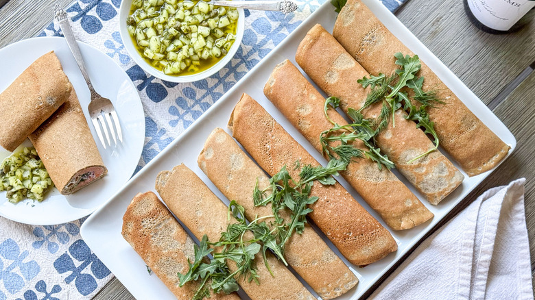 Buckwheat crepes with salmon and homemade creme fraiche on serving platter with arugula and cucumber dressing