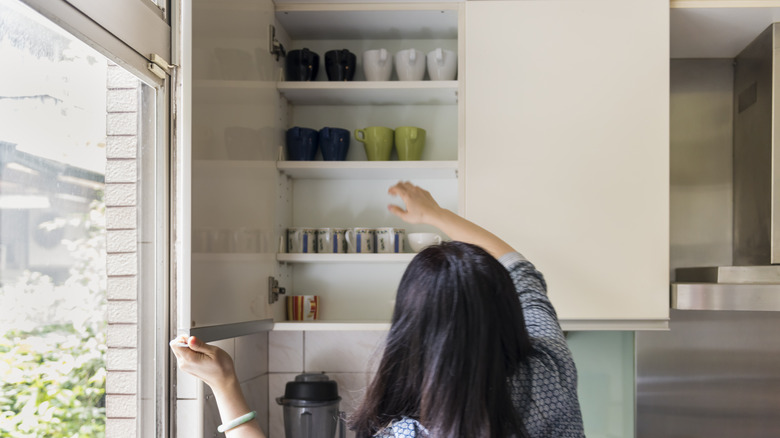 Woman reaching for cup in kitchen cabinet