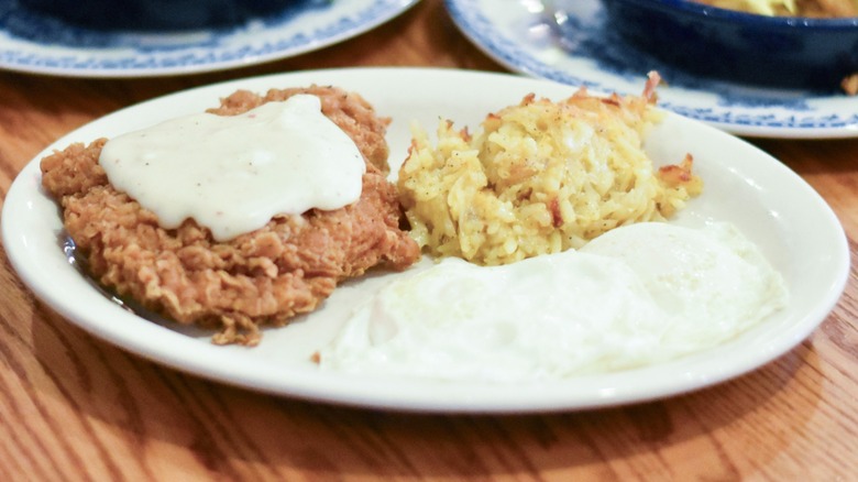 A fried chicken steak with white gravy and hashbrown casserole on a white plate