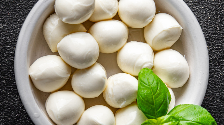A white bowl of mozzarella cheese balls with a basil leave garnish