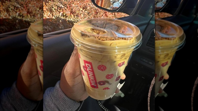 A woman holding a Dunkin' Cookie Butter Cold Brew in her car