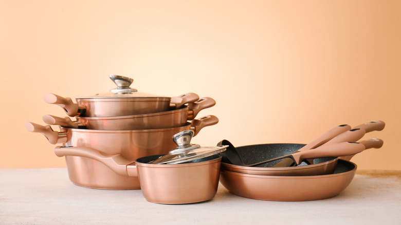 Set of copper pans on table against color background