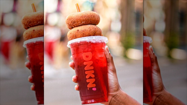 Someone holding a Cranberry Apple Refresher with two donuts perched on top of the drink