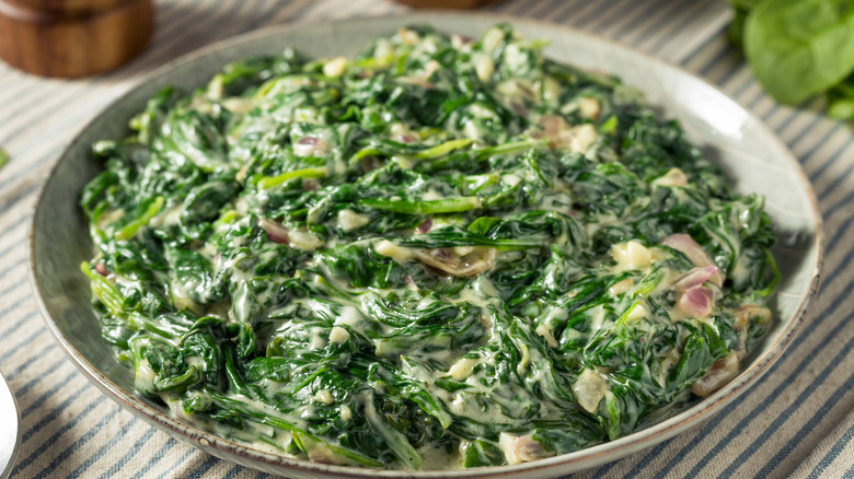 A bowl of super fresh creamed spinach over a striped tablecloth.