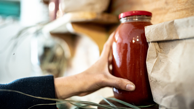 A woman getting a jar of pasta sauce off of a shelf