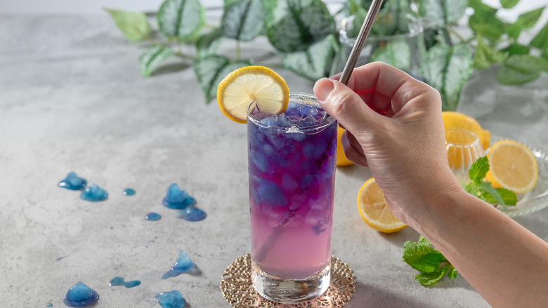 A tall glass of purple butterfly pea flower tea with a metal straw.
