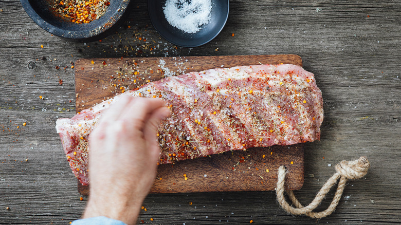 hand sprinkles salt and dry rub on ribs
