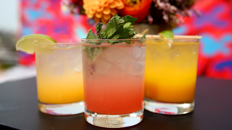 Three different types of mocktails with a bouquet of flowers in the background.
