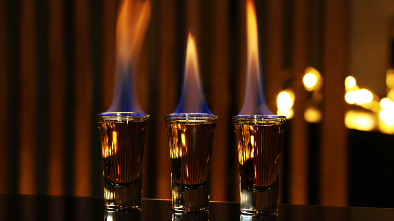 3 shot glasses with brown liquid lit on fire