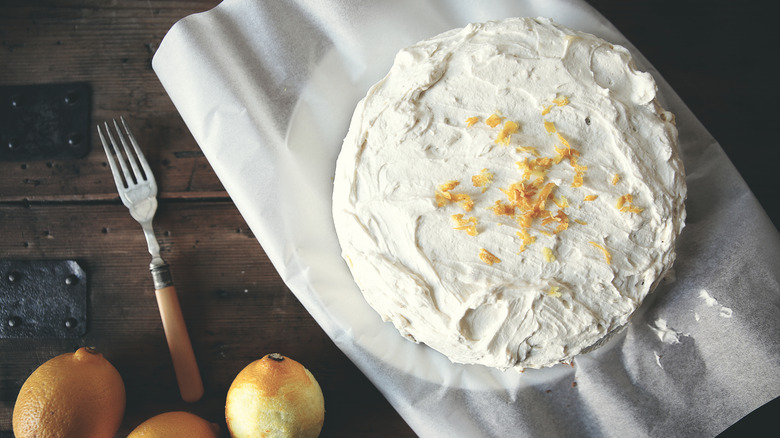 Cake with frosting topped with lemon zest on plate covered with parchment paper