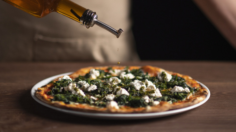 Person drizzling oil on top of a pizza