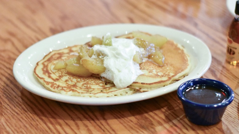 A white platter with pancakes, apple topping, and whipped cream