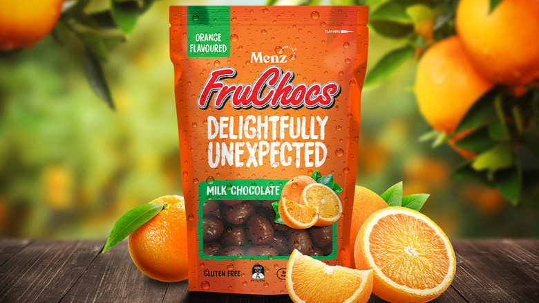 A bag of FruChocs orange flavor on a table with oranges