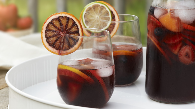 Two glasses and a pitcher filled with sangria on a white platter.