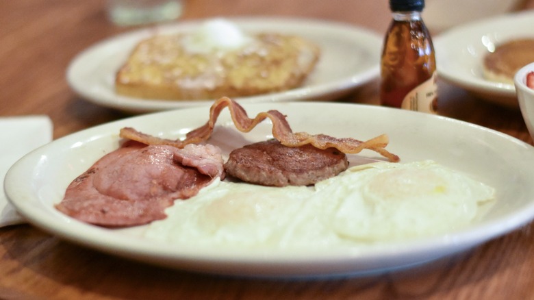 A white plate with eggs, ham, sausage, bacon, and French toast