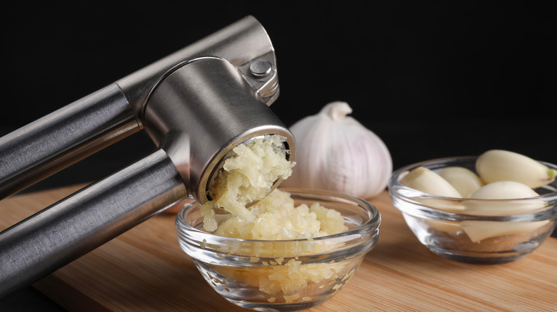 Crushing garlic with press into bowl at wooden table, closeup