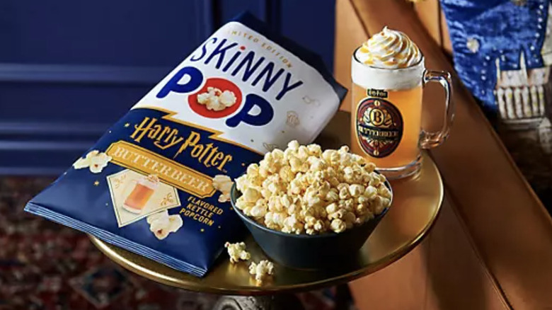 A bag of SkinnyPop Harry Potter Butterbeer popcorn on a table next to a bowl of the popcorn and a mug of butterbeer