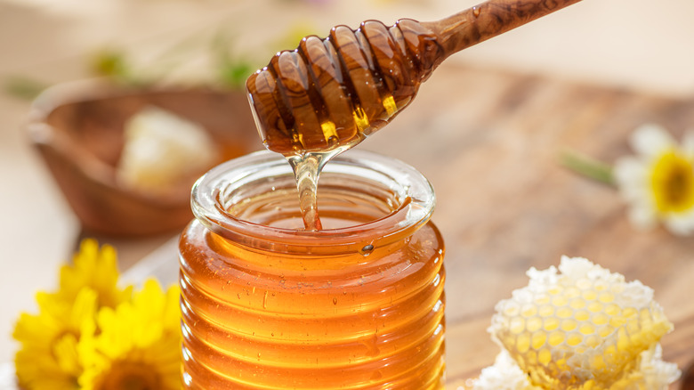 A jar of honey with a honey stick dripping