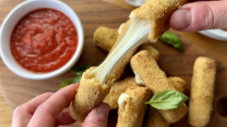 hand holding two parts of a mozzarella stick above a bowl of tomato sauce
