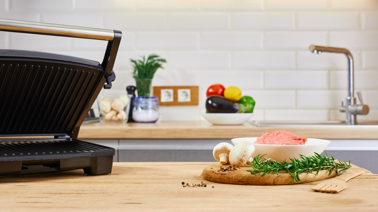 Food next to a panini press on a kitchen counter
