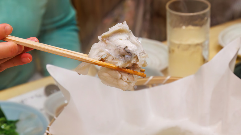 A piece of blowfish, being held by chopsticks